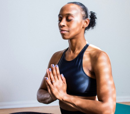 Black woman wearing her hair in a bun while sitting on the floor in a prayer position 